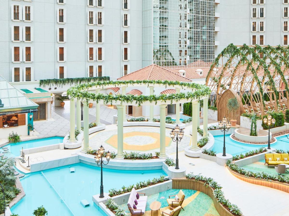Hotel Grand Nikko Tokyo Bay Maihama Urayasu Exterior foto The photo shows a beautifully landscaped outdoor area, likely part of a resort or hotel. It features a central circular structure supported by white columns, decorated with greenery. Surrounding this structure are several swimming pools or water feat