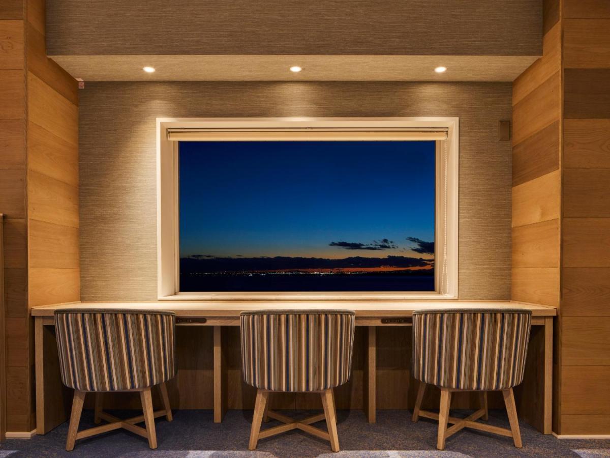 Hotel Grand Nikko Tokyo Bay Maihama Urayasu Exterior foto The photo depicts a cozy workspace or study area featuring a long, minimalist desk with three chairs. The wall behind the desk is made of wood, creating a warm atmosphere. At the center, there is a large window that showcases a beautiful evening view