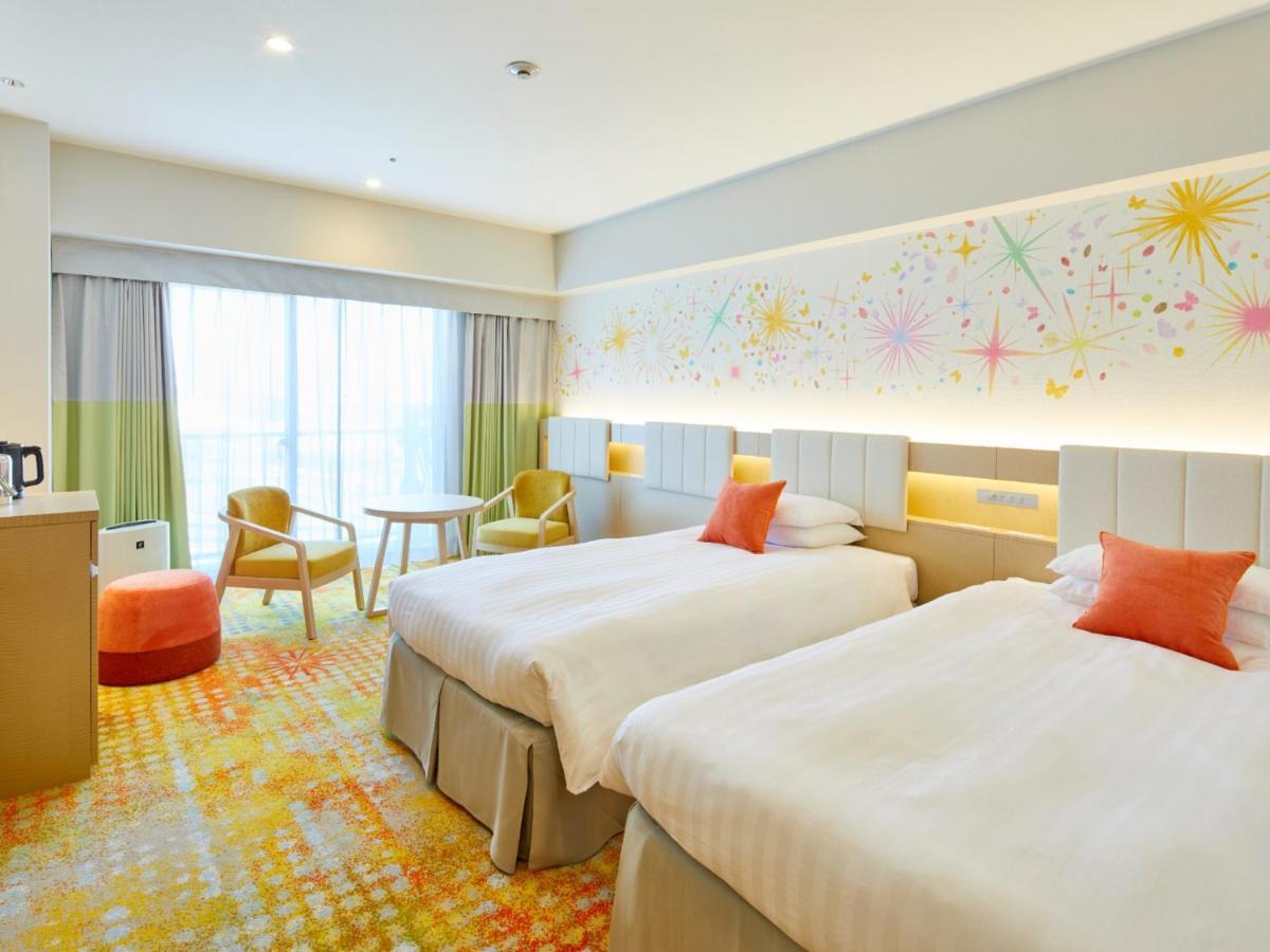 Hotel Grand Nikko Tokyo Bay Maihama Urayasu Exterior foto The photo shows a modern hotel room featuring two twin beds with light-colored bedding and decorative orange cushions. There is a vibrant, colorful carpet on the floor, and the walls are adorned with playful designs, including bursts of color. A larg