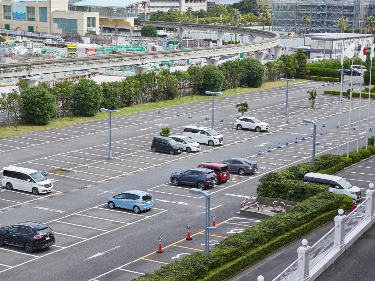 Hotel Grand Nikko Tokyo Bay Maihama Urayasu Exterior foto The photo shows a partially empty parking lot with several parked cars. In the foreground, there are a few vehicles, including a blue car and a white one. The lot has clearly marked parking spaces, and there are some trees and shrubs along the sides.