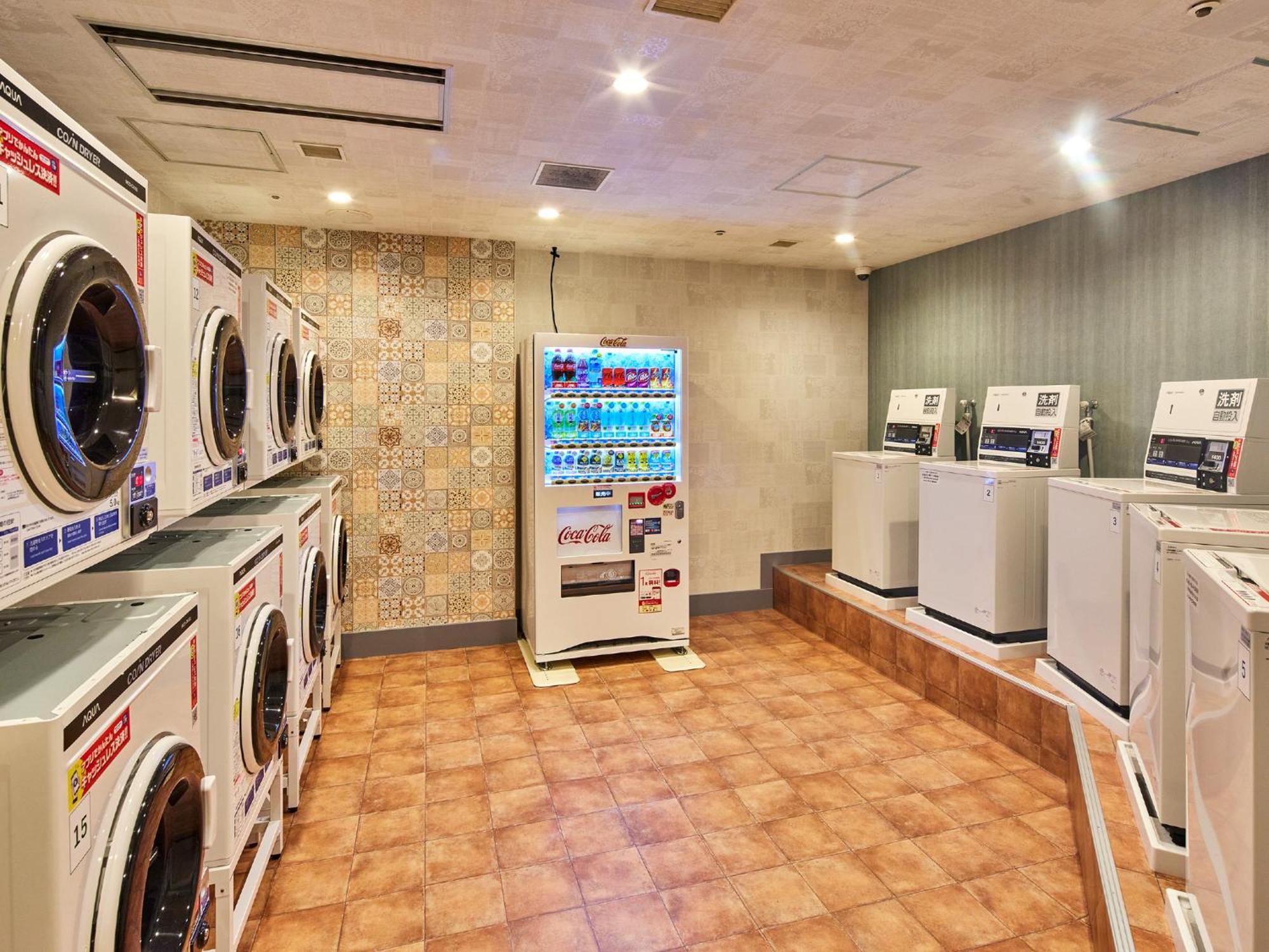 Hotel Grand Nikko Tokyo Bay Maihama Urayasu Exterior foto The photo shows a laundry room equipped with several washing machines and dryers. On the left side, there are multiple front-loading washing machines arranged in a row, and on the right side, there are dryers. In the center, there is a vending machin